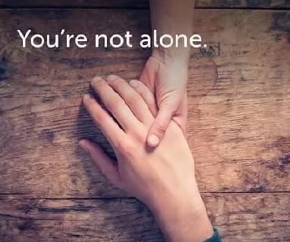 Two hands holding each other on a wooden table, with the words 'You're not alone'