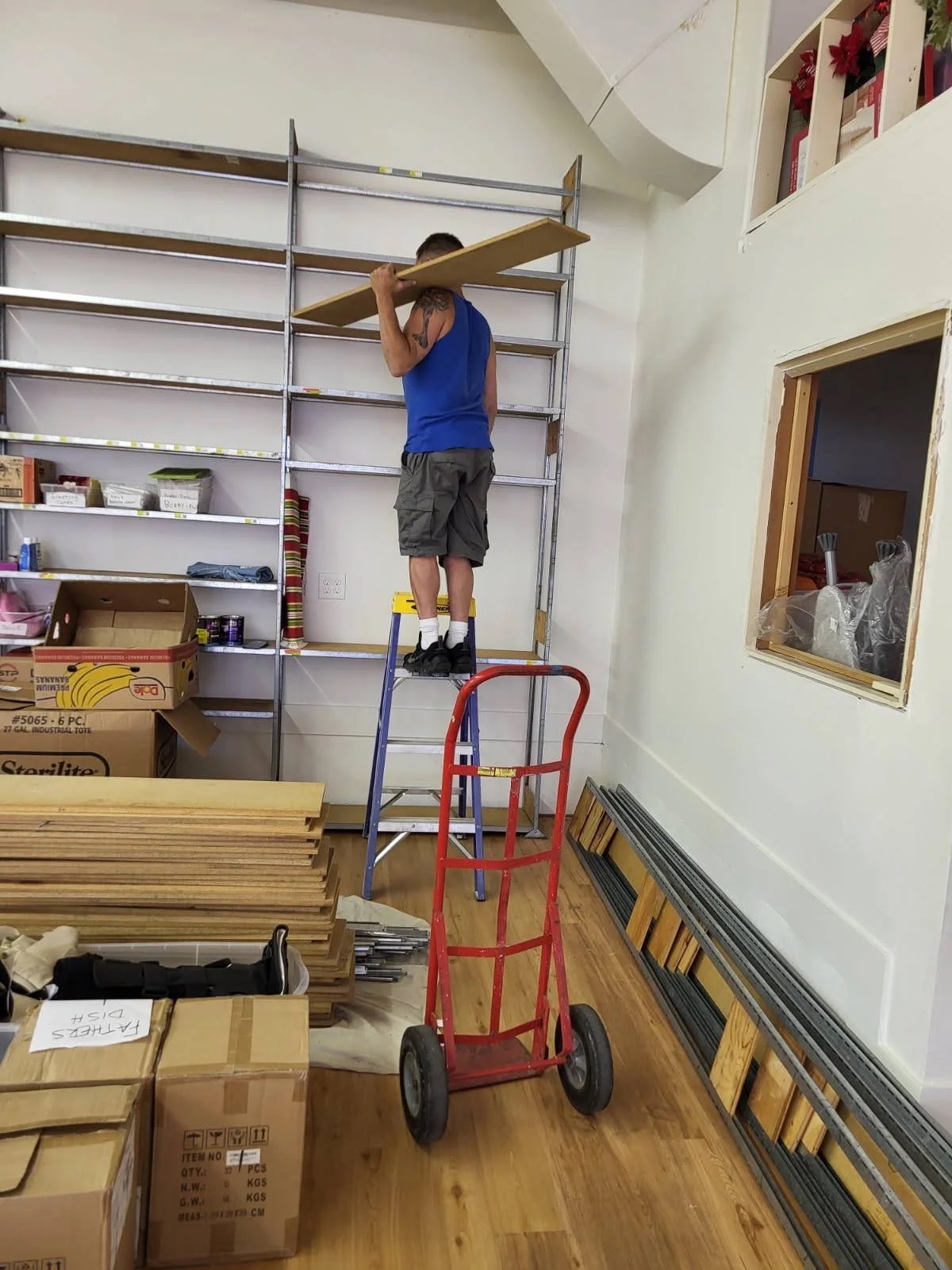 A volunteer on a step stool assembling shelving in the new Gg's House building